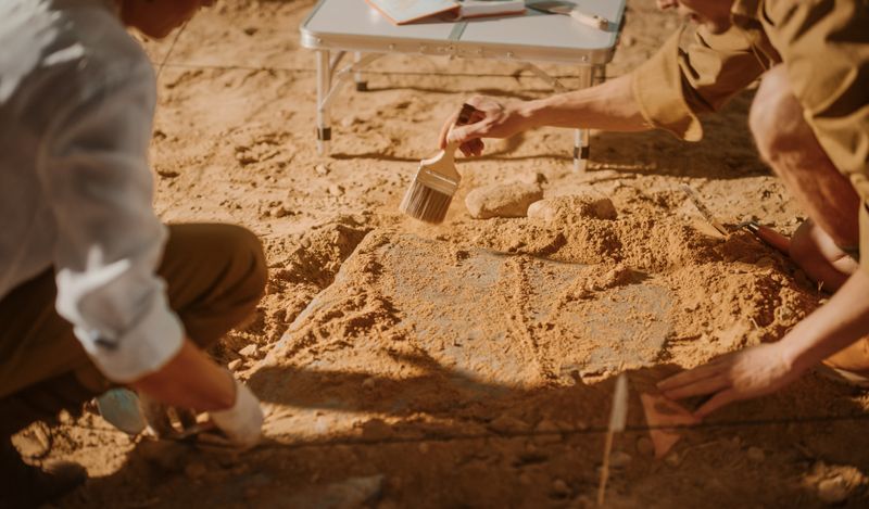 Image of someone looking for something carefully in the sand using a paintbrush