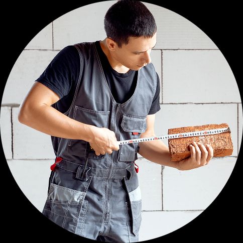 A builder measuring a brick with a tape measure.