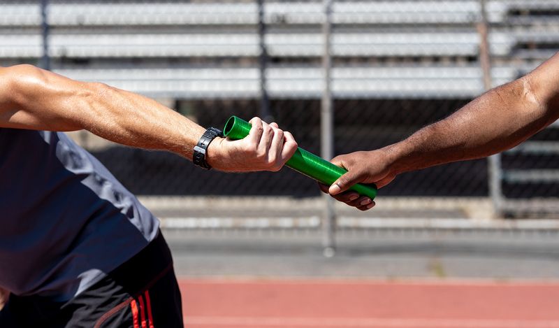 Two hands passing a baton in a relay race, representing the continuous handoff between stages in the agile software development lifecycle