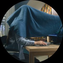 person at a desk hiding under a blanket